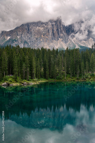 Fototapeta Naklejka Na Ścianę i Meble -  Extremely clear water with reflection in Carezza lake in South Tyrol, Italy. Surrounded by green , rich forest and dolomite mountains, Alps.