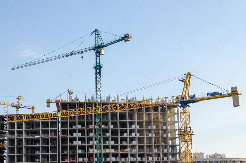 The construction site with four cranes and two unfinished buildings on a sunny day with clear sky and copy space 