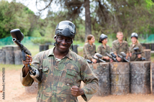Smiling afro american man paintball player in camouflage posing with gun outdoors