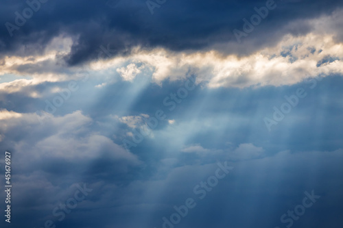 Sunbeams breaking through dark clouds. Stormy sky and sun rays. Epic view of natural background. © olga_gl