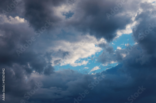 Part of blue sky look through frame of dark clouds. Beautiful natural air background. © olga_gl