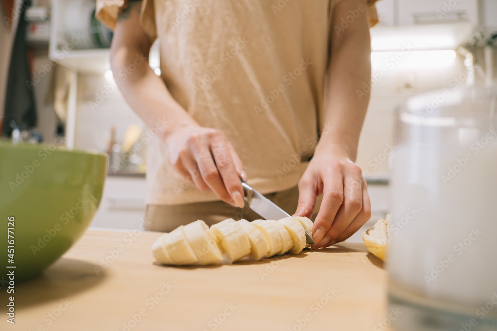 Young woman slices a banana to make a granola and yogurt breakfast.