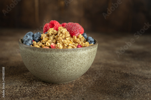 Granola bowl with strawberry and blueberry on the brown rustic wooden background, summer superfood breakfast concept, hero view