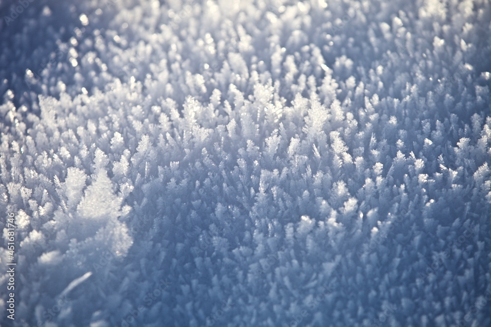 White ice crystals in bright sunlight. Macro photography of ice crystal texture. Snow crystals close-up on a bright frosty winter day. White sparkling snow surface close up. Abstract snowy pattern.
