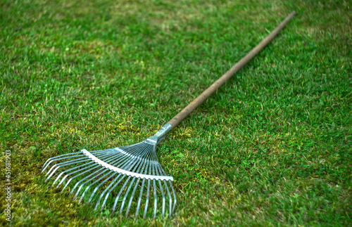 Photo Metal rake with a wooden handle on the green grass in the garden
