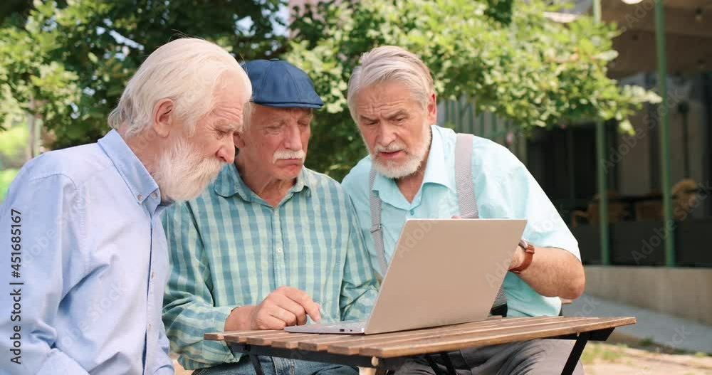 Waist up portrait view of the three joyful childhood friends gathered together in outdoor cafe and using laptop computer with interest. Friendship concept Waist up portrait view of the three joyful childhood friends gathered together in outdoor cafe and using laptop computer with interest. Friendship concept