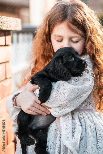 Little red hair girl hugging her new friend  cute black puppy
