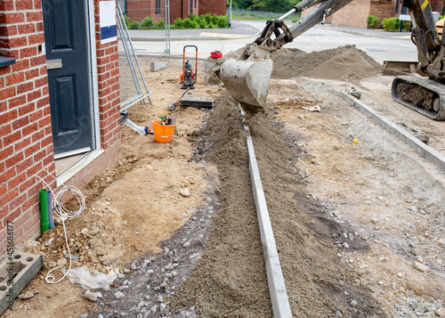 Installation of edging kerb during footpath construction in front of new build house on new housing  development and placing semidry concrete around it with excavator. photo