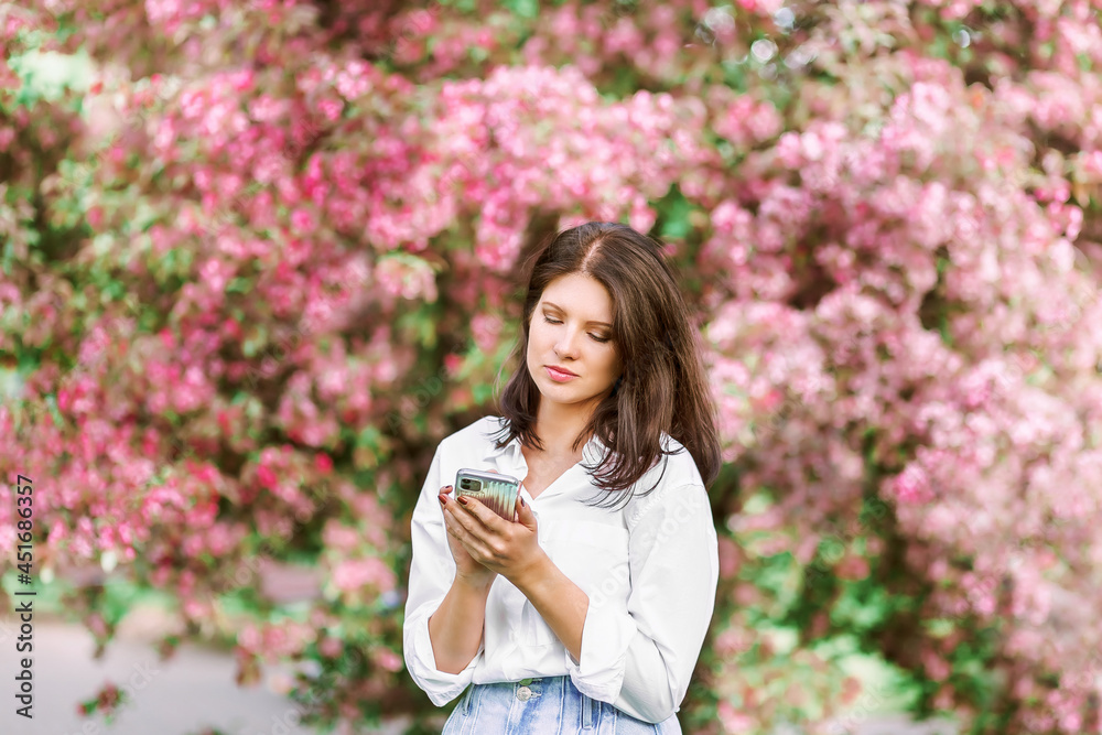 Woman with phone outdoors. Girl with pink coat using mobile in park.