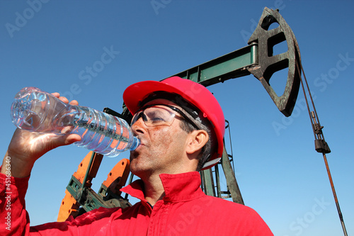 Oil worker drinking clean water from plastic bottle at oil well in the hot desert photo