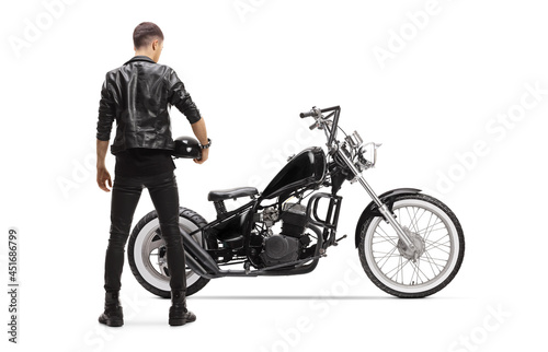 Rear view of a biker in a leather jacket with a chopper holding a helmet