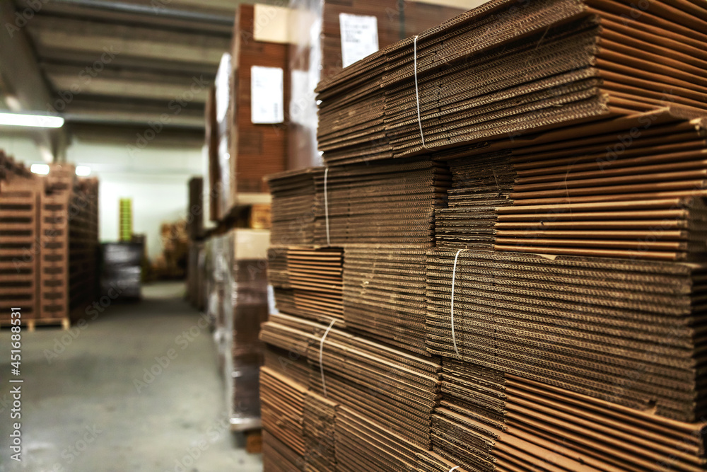 Obraz premium Storage with stocks of unpacked cardboard boxes for packing goods. Large empty hall without people with a lot of cardboard. Stocks of raw materials for package distribution and logistics