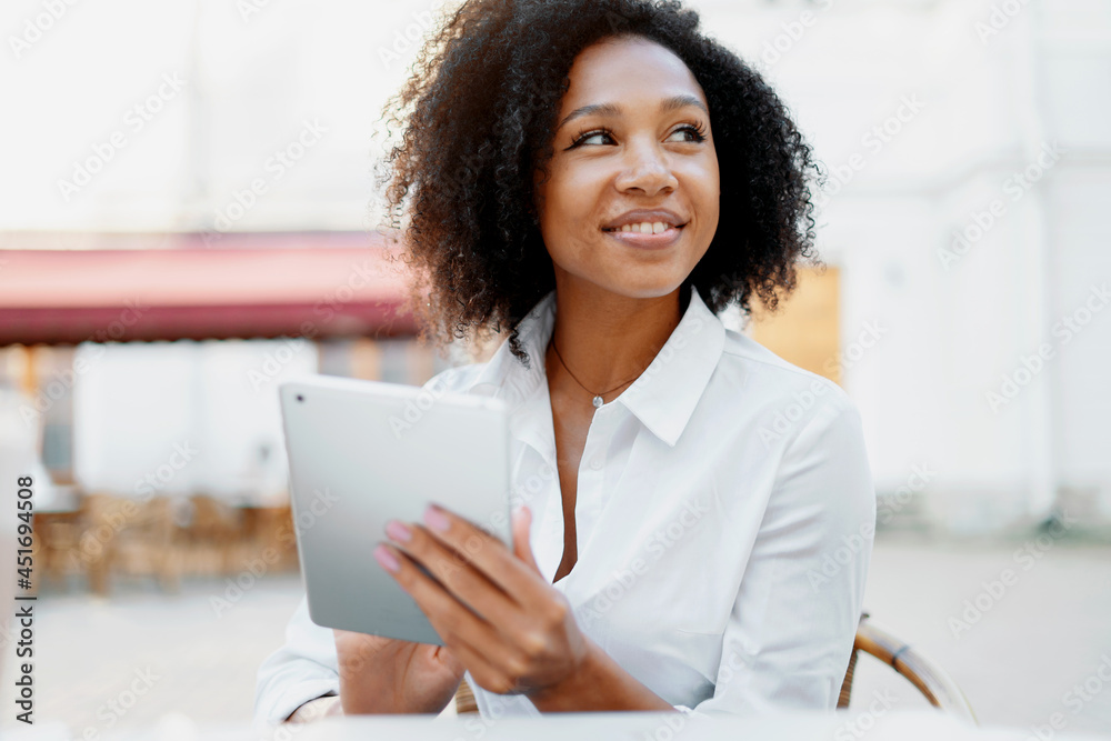 A beautiful Afro-looking woman is surfing the Internet on a tablet in a summer cafe. The student does the task online for the new course of the lesson. A beautiful Afro-looking woman is surfing the Internet on a tablet in a summer cafe. The student does the task online for the new course of the lesson.