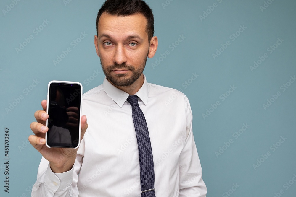 Closeup photo of Handsome happy cool young man good looking wearing casual stylish clothes standing isolated over colourful background wall holding smartphone and showing phone with empty screen Closeup photo of Handsome happy cool young man good looking wearing casual stylish clothes standing isolated over colourful background wall holding smartphone and showing phone with empty screen