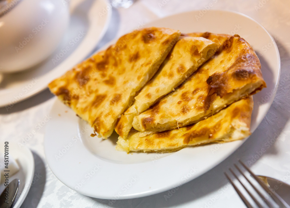 Freshly baked khachapuri bread with melted burnt cheese on a white plate in a restaurant