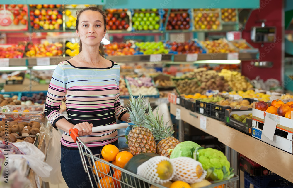Portrait of cheerful woman buyer choosing fruits at store.