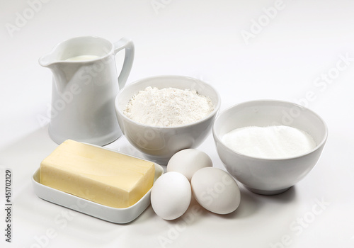 Ingredientes para bolo, ovos, farinha de trigo, açúcar, leite e manteiga no fundo branco para recorte.
 photo