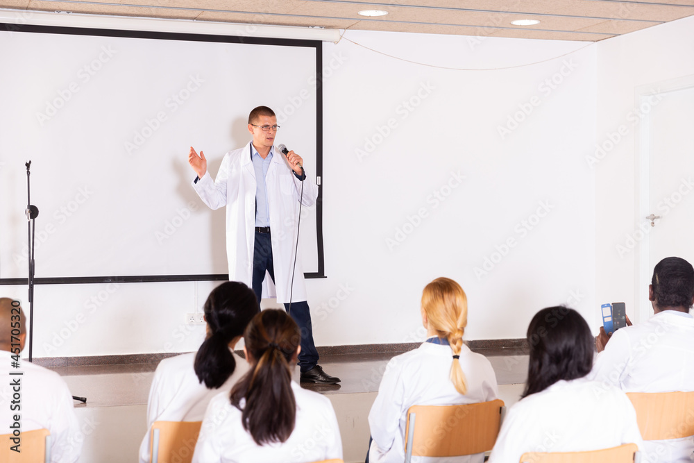 Confident male speaker in white coat giving presentation from stage at ...