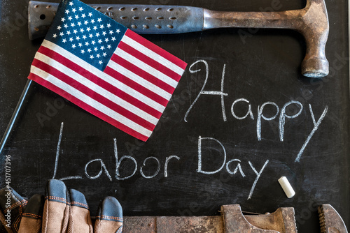 Happy Labor Day message written in white chalk on a black chalkboard with American flag and tools