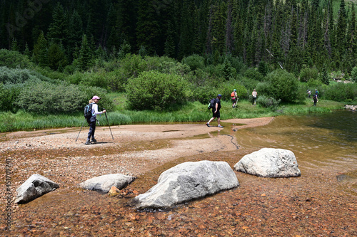 Hikers cross shallow water of Upper Urad Reservoir on Hassell Lake Trail in Arapaho National Forest, Colorado on sunny summer afternoon. photo