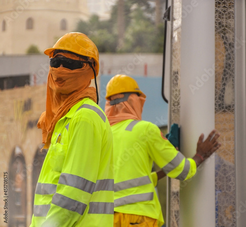 Two blue-collar workers wearing helmets and yellow jackets working under the heat in Doha, Qatar. 