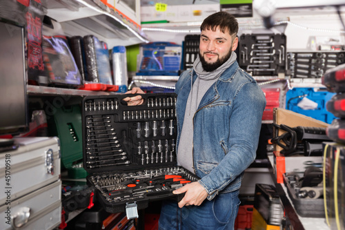 Glad positive smiling worker chooses set of tubular keys and set of heads for work in tools store photo