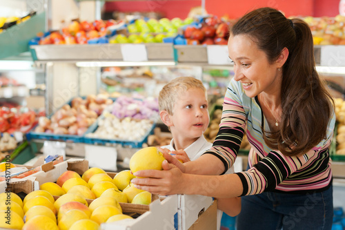 Cheerful boy with his mother choosing fresh pears and apples at fruit department of supermarket