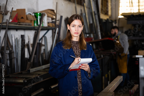 Mechanical metalworking factory workwoman noting measurement or order data in notebook.. photo