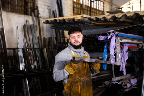 Skilled locksmith working in mechanical metalworking shop, preparing shaped tubes for cutting.. photo