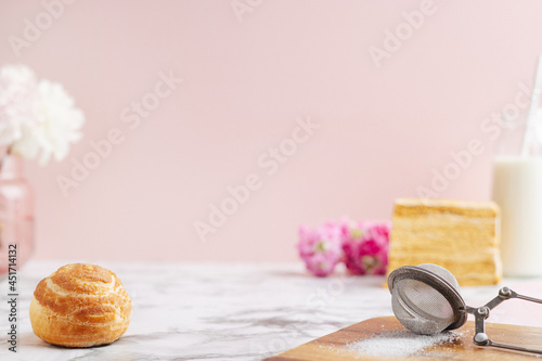 Homemade profitroles pastry filled with custard. Eclairs with cream, French dessert and flowers on marble table on pink background photo