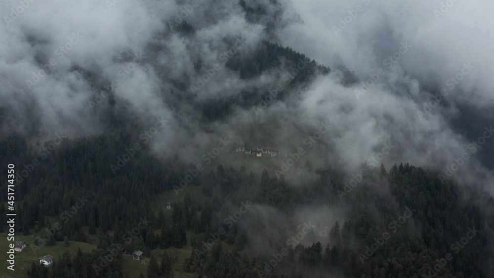 drone aerial view of a cloud of fog rising up the side of a mountain, hiding a small village underneath, dark mood scene drone aerial view of a cloud of fog rising up the side of a mountain, hiding a small village underneath, dark mood scene