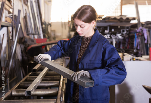 Young woman worker with metal beams during work in workshop