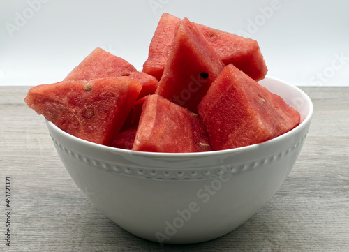 Watermelon slices in a white bowl on wooden table. Fresh fruit