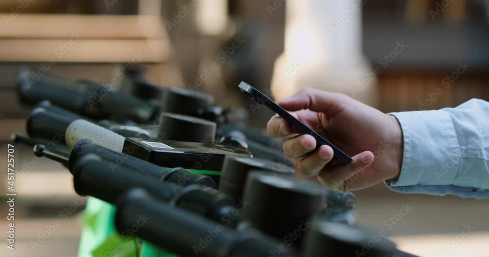 A man brings a mobile phone to the handle of the electric kick scooter and moves his finger across the smartphone screen, activates the electric kick scooter.