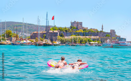 Girls in bikini lying on air bed in the turqouise sea  - Panoramic view of Saint Peter Castle (Bodrum castle) and marina - Bodrum, Turkey © muratart