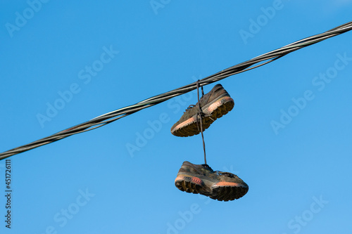 Old torn shoes for athletic running hang on a city street on electrical wires. The concept of hazardous disposal of worn-out footwear, harm of garbage to humans and the environment.