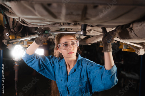 Young beautiful woman car mechanic is dressed in safety glasses and working overalls turns a nut for wrenches.