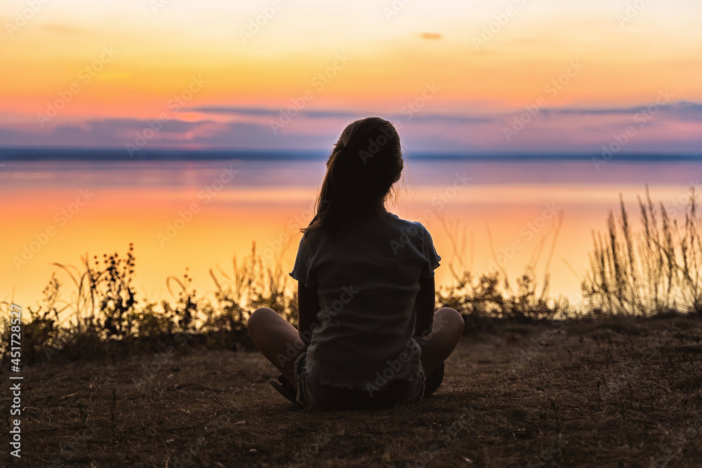 The silhouette of a little girl on the shore in front of a colorful orange sunset over the sea The silhouette of a little girl on the shore in front of a colorful orange sunset over the sea