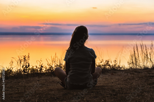 The silhouette of a little girl on the shore in front of a colorful orange sunset over the sea