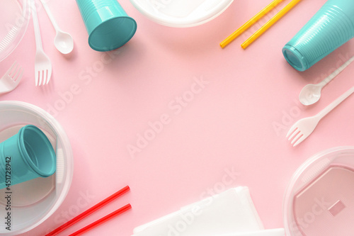 Frame of various disposable plastic tableware on pink background, space for text