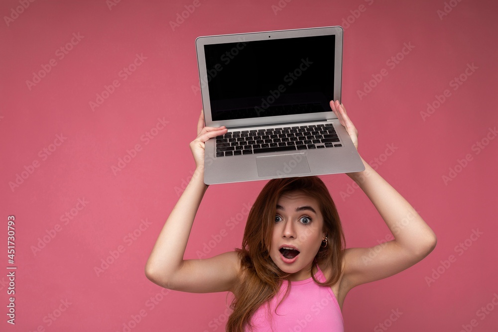 Naklejka premium Close-up portrait of Beautiful amazed young woman saying wow with open mouth holding netbook computer looking at camera