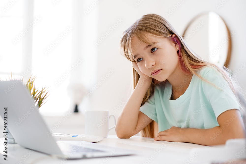 Obraz premium Happy little girl pupil using laptop at home