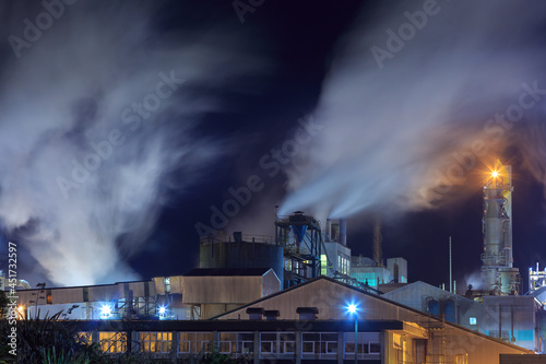 Steam billows from the chimneys of a pulp and paper mill at nighttime