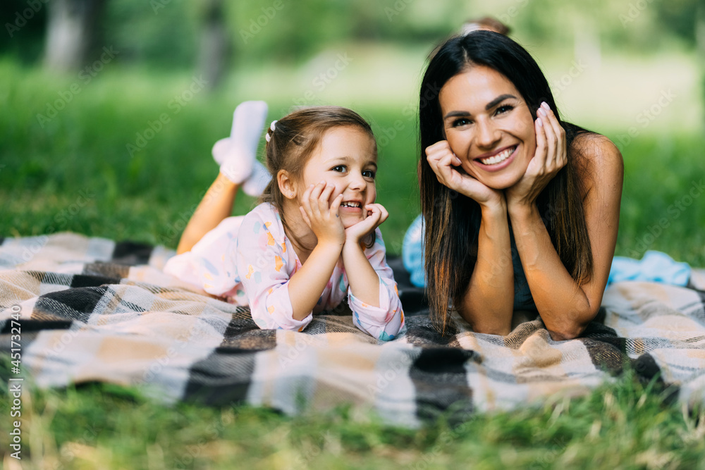 Portrait of smiling mother and child lying together on a green grass in summer park Portrait of smiling mother and child lying together on a green grass in summer park