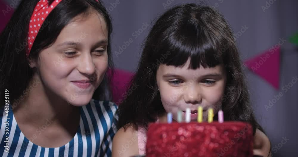 Two girls are sitting near a birthday cake with candles and eagerly want to take a bite of it. 50 fps slow motion 4k Two girls are sitting near a birthday cake with candles and eagerly want to take a bite of it. 50 fps slow motion 4k