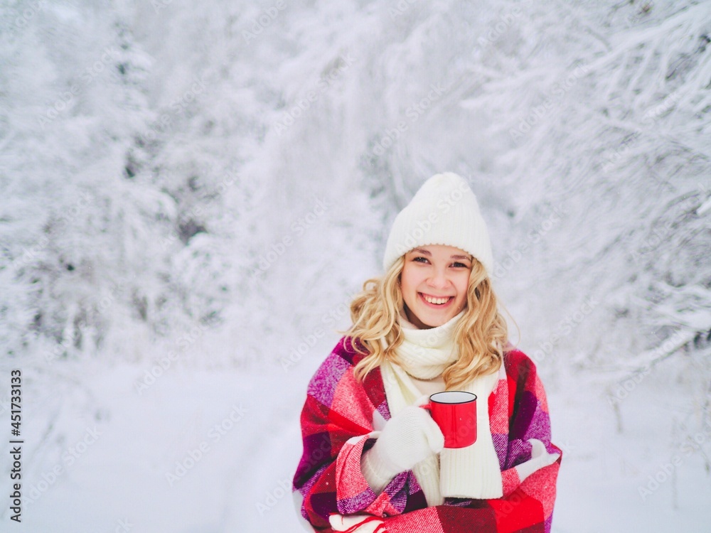 Obraz premium Beautiful happy smiling young woman in red plaid with cup of hot drink on cold snowy winter outdoors. Girl hands in gloves holding mug with hot cocoa, tea, coffee. Winter, Christmas time