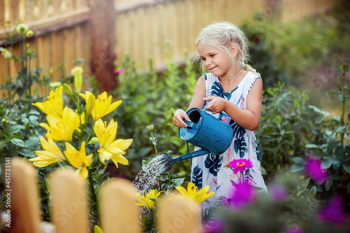 a girl waters flowers, a lily, a garden, a young florist, summer in the village, joy, happiness, children, a front garden, a new wooden fence