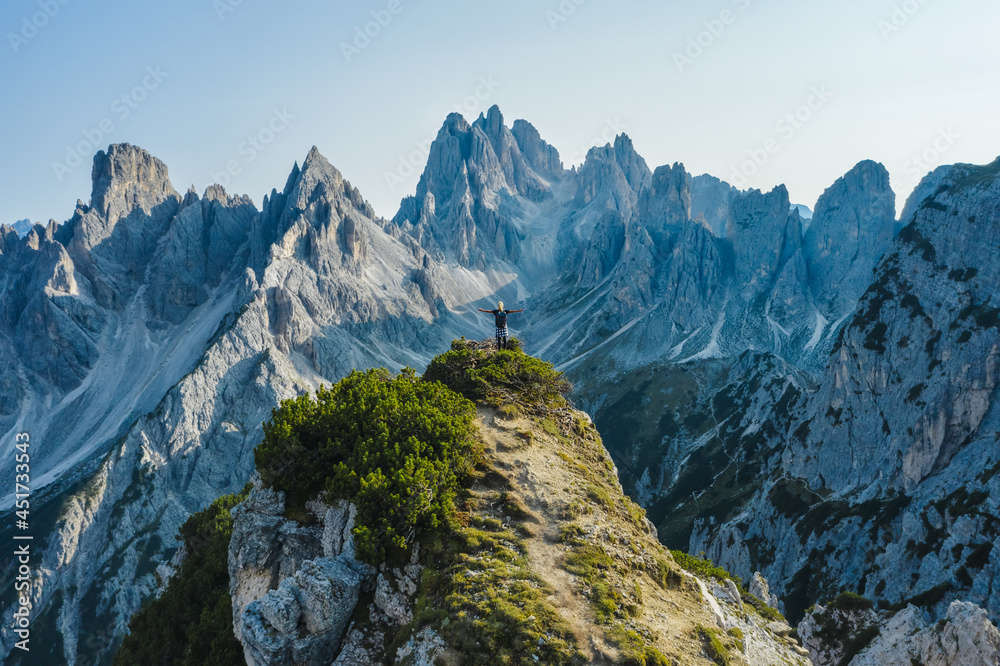 Aerial view of a woman hiker raising her hands on mountain top enjoying Cadini di Misurina mountain peaks, Italian Alps, Dolomites, Italy, Europe