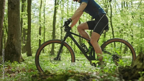 A man on an MTB bike is riding through the forest. He is training before the competition. The camera is shooting from the side and moving with him. 4K