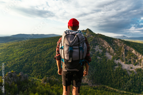 A traveler on the background of mountains. A tourist with a backpack is standing on the top of the mountain. A man with a backpack in the mountains at sunset, rear view. Domestic tourism. Copy space